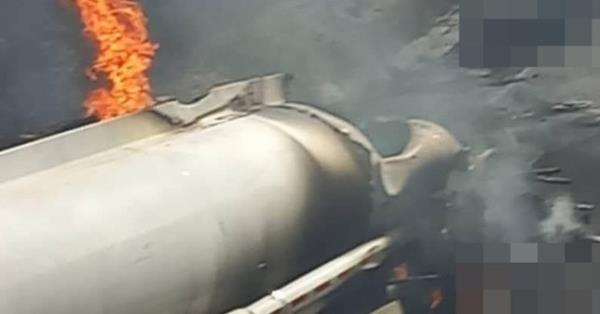 Fire emerges from a charred fuel tanker with a hole ripped into it by the explosion.